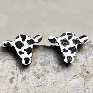 Detailed close-up of cow head earrings with black and white spotted cow print on stone