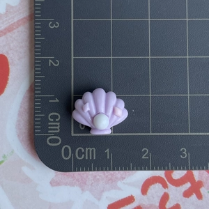 Vue détaillée d'une breloque coquillage violette en résine avec perle sur une règle