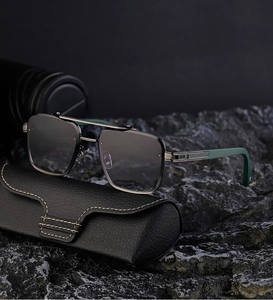 Close-up of rimless square sunglasses with green temples on a rugged stone base