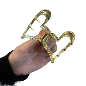 Elegant gold metal heart-shaped hair claw clip for women held against a white background