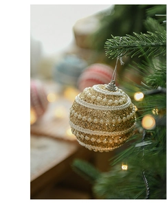 Detail of an 8cm gold sequin Christmas ball with white pearls on a green tree branch