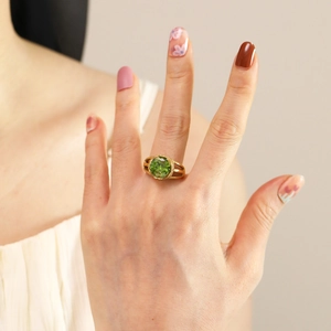 Detailed view of 18K gold plated ring with green zircon on woman's middle finger
