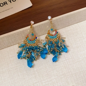 Macro detail of bohemian gold-plated teardrop earrings with blue beaded tassels and rhinestones