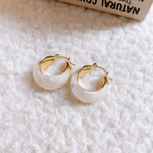 Detail of U-shaped gold earrings with white marble resin on white plush fabric