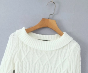 Detail of white cable knit sweater texture showing thick braided pattern on wooden hanger