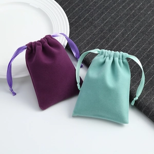 Purple and mint green velvet drawstring jewelry pouches on a minimalist white tray