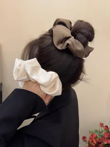 Detail of oversized satin scrunchies in coffee and cream on a bun and low ponytail