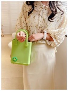 Nahaufnahme der lindgrünen Mini-Tasche mit Blumenanhänger, gehalten von einem Model