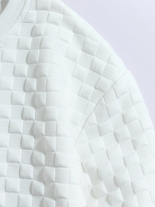 Close-up of white long sleeve top featuring textured quilted grid fabric and ribbed neckline