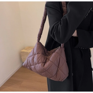 Detail of a dark coffee quilted puffer shoulder bag worn by a model in a minimalist room
