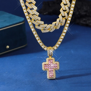 Close-up of golden Cuban link chain and pink diamond cross pendant on blue velvet
