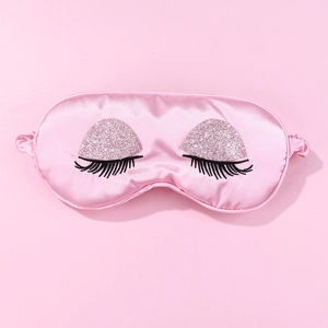 Detailed view of pink satin sleep mask with embroidered long eyelashes and glitter finish