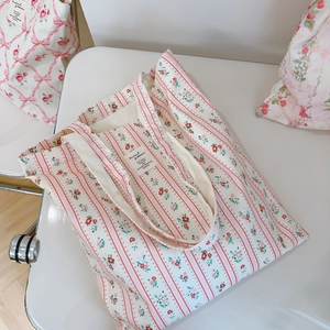 Detail view of cotton tote bag with pink floral stripes and woven label on a white chair