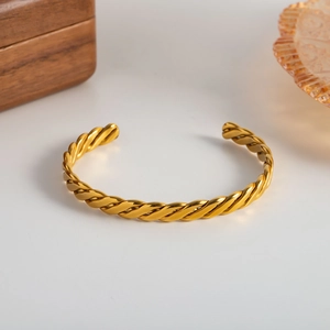 Detailed view of the 18K gold plated twisted rope cuff bangle on a white surface