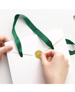 Applying a gold rose wax seal sticker to a white paper gift bag with green ribbon handle