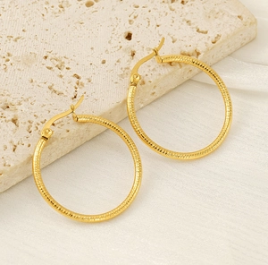Detailed macro view of large golden hoop earrings with textured spiral surface on stone