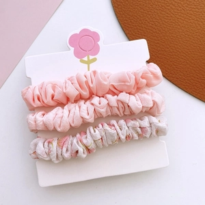 Trois chouchous en tissu rose et fleuri présentés sur une carte papier décorative