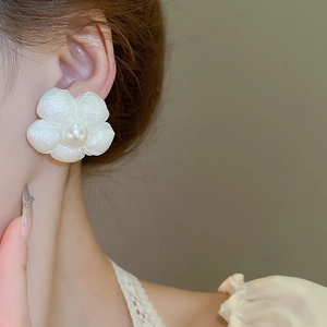 Close-up of white five-petal flower earring with pearl center worn on female ear