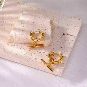 Detail of gold geometric T-bar pendant earrings on natural stone texture background