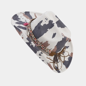 Detail of cow print cowboy hat featuring woven band and pink tassel accessories