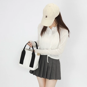 Detail of white canvas tote bag with black contrast handles and leather brand patch