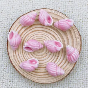 Close-up of pink spiral ceramic shell charms for DIY jewelry on a wooden tray