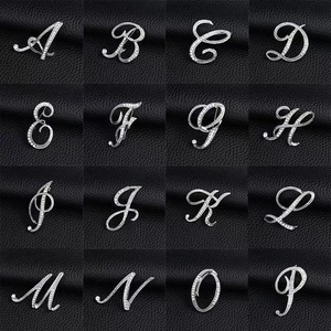 Macro view of silver rhinestone initial brooches in elegant script on black leather