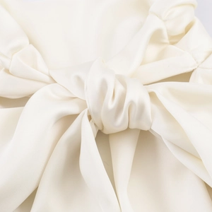 Close-up of cream satin blouse showing soft fabric texture and elegant bow detail