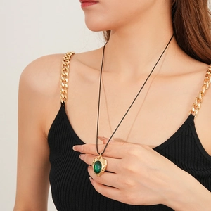 Detailed view of vintage gold heart pendant with green gemstone on a black cord