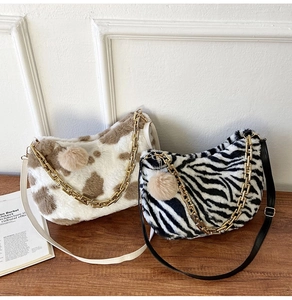 Close-up of cow and zebra print plush tote bags with metal chains and fluffy pom charms