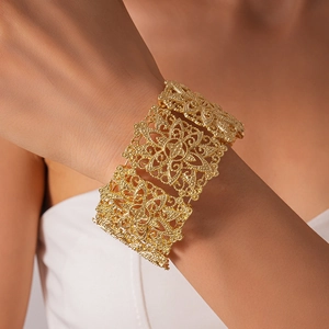 Vue détaillée du large bracelet manchette à fleurs filigranes dorées au poignet du mannequin