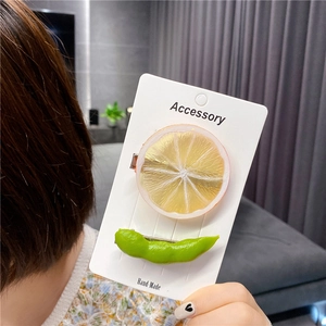 Realistic lemon and edamame hair clips displayed on an accessory card by a model