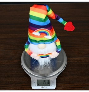 Rainbow striped gnome plush weighing 143.8g on a digital scale for size reference