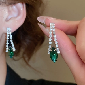 Detailed view of silver-toned drop earrings with green zircon tassels on model