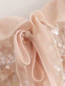 Detail of ruffle trim and sequins on beige-pink sleeveless top with bow tie accent