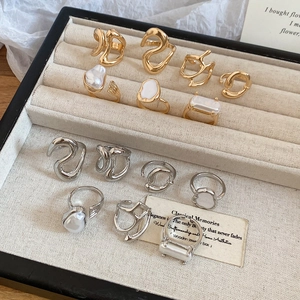 Flat lay of gold and silver metal rings with irregular pearls on a beige jewelry tray