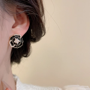 Close-up of black camellia flower earrings with pearl accents on a female model