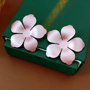 Gros plan de boucles d'oreilles fleurs roses mates sur fond de boîte cadeau verte