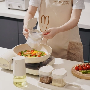 Waterproof kitchen apron worn by a woman using glass seasoning jars in a modern kitchen decor