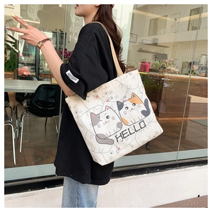 Close-up of a beige canvas tote bag with cartoon cat patterns and HELLO print