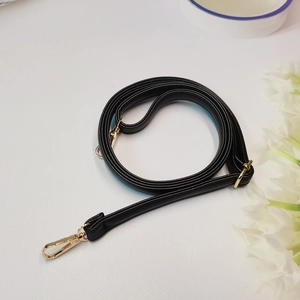 Detalle de correa ajustable de cuero negro granulado con mosquetones dorados brillantes