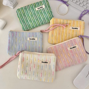 Flat lay of colorful woven mini makeup bags with zippers on a white desk workspace