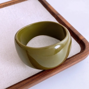 Gros plan d'un large bracelet en résine acrylique vert olive sur une surface en tissu