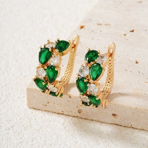 Elegant gold earrings with green and white gemstones on natural stone background