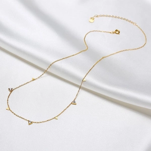 Detail of gold titanium necklace with triangle zircon pendants on white silk background