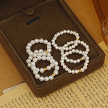 Macro shot of six elastic pearl rings with gold beads on brown velvet in vintage setting