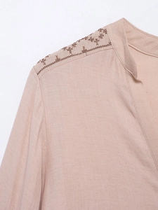 Macro detail of floral embroidery on the shoulder of a linen V-neck long sleeve blouse