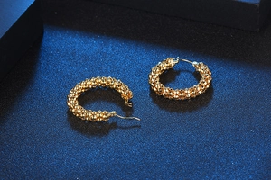 Close-up of golden hoop earrings featuring intricate beaded texture on a dark background
