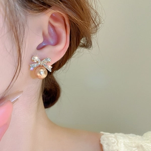 Détail de boucles d'oreilles nœud doré avec strass brillants et une perle suspendue