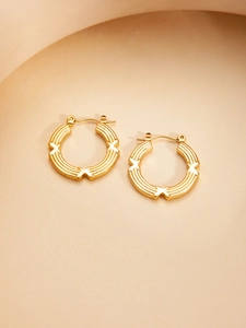 Macro detail of gold-plated hoop earrings with engraved X motifs and triple groove textures